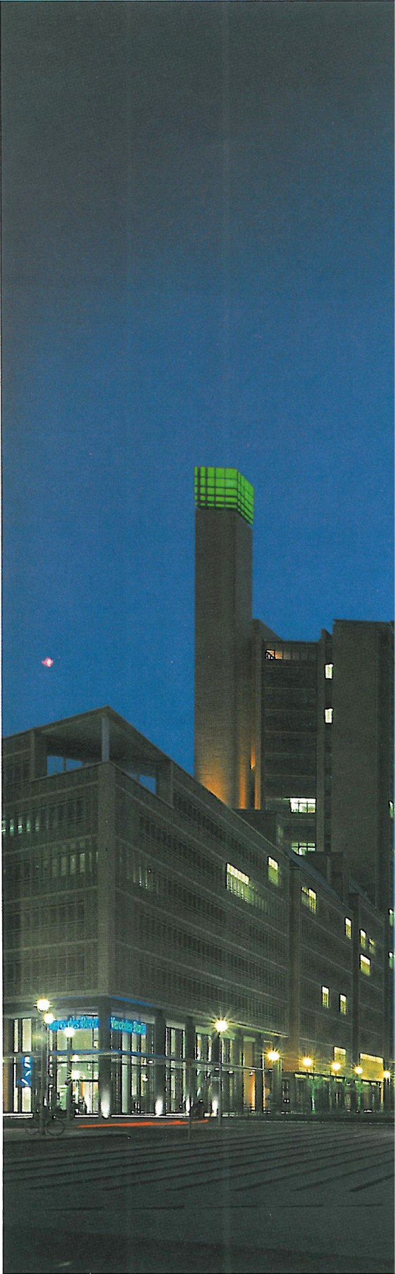 Night view of the Piano–Kohlbecker tower from street level, with the green beacon glowing at top