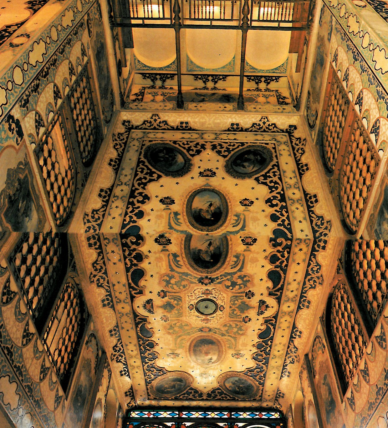 Looking up into a fully restored Esfahani painted vault: floral and arabesque patterns cover the surface above a stained-glass orosi window at the base.