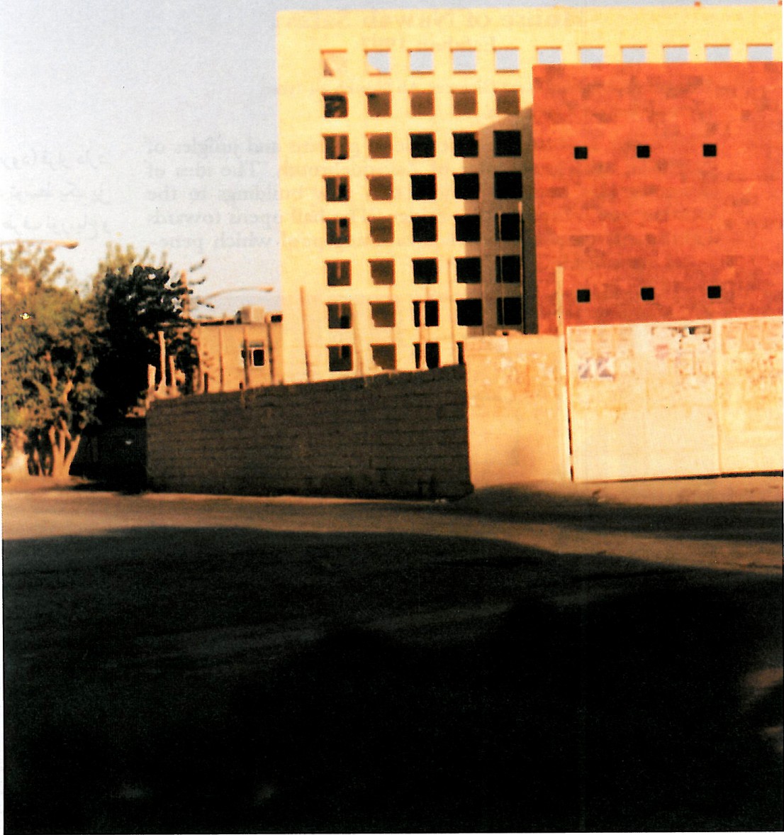 Close view of the Esfahan Library's perforated brick wall and corner stair tower, partly hidden behind dark green branches in the foreground.