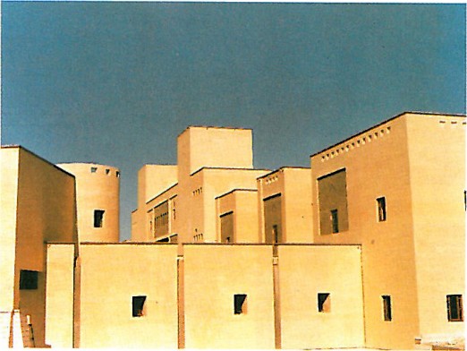 Yellow-brick faculty building with stepped massing, photographed against a clear blue Yazd sky.