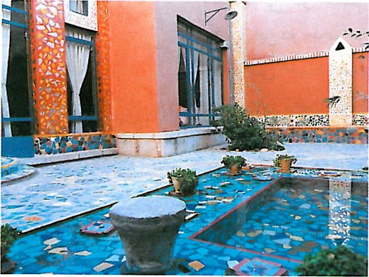 Inward-looking residential courtyard: a stepped concrete fountain at centre, red-brick perimeter walls and potted plants arranged around the basin.