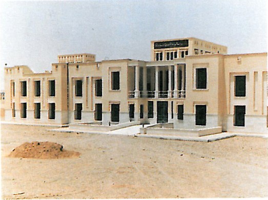 Long two-storey rectangular dormitory building of warm buff-coloured brick with regular fenestration, in late-afternoon shadow on a Yazd campus.