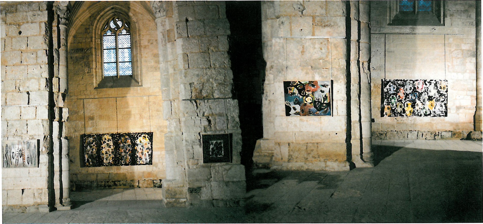 Installation view of Zenderoudi's mosaic-like wall works inside a Romanesque stone interior in Bernay, France, with framed colourful panels mounted on weathered stone walls.