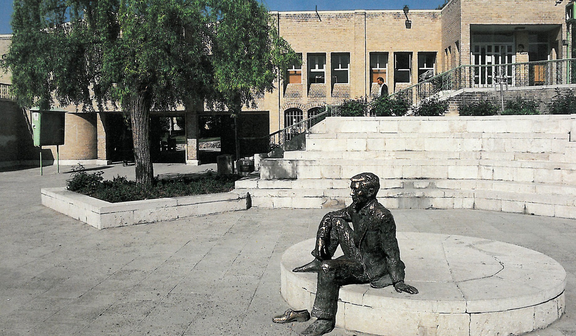 Photograph of Park Shafagh's main plaza with a bronze Tanavoli sculpture of a seated figure on a circular base in front of a brick library building