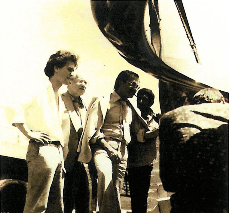 Sepia-toned photograph of Kamran Diba with a sculpture and classmates in conversation