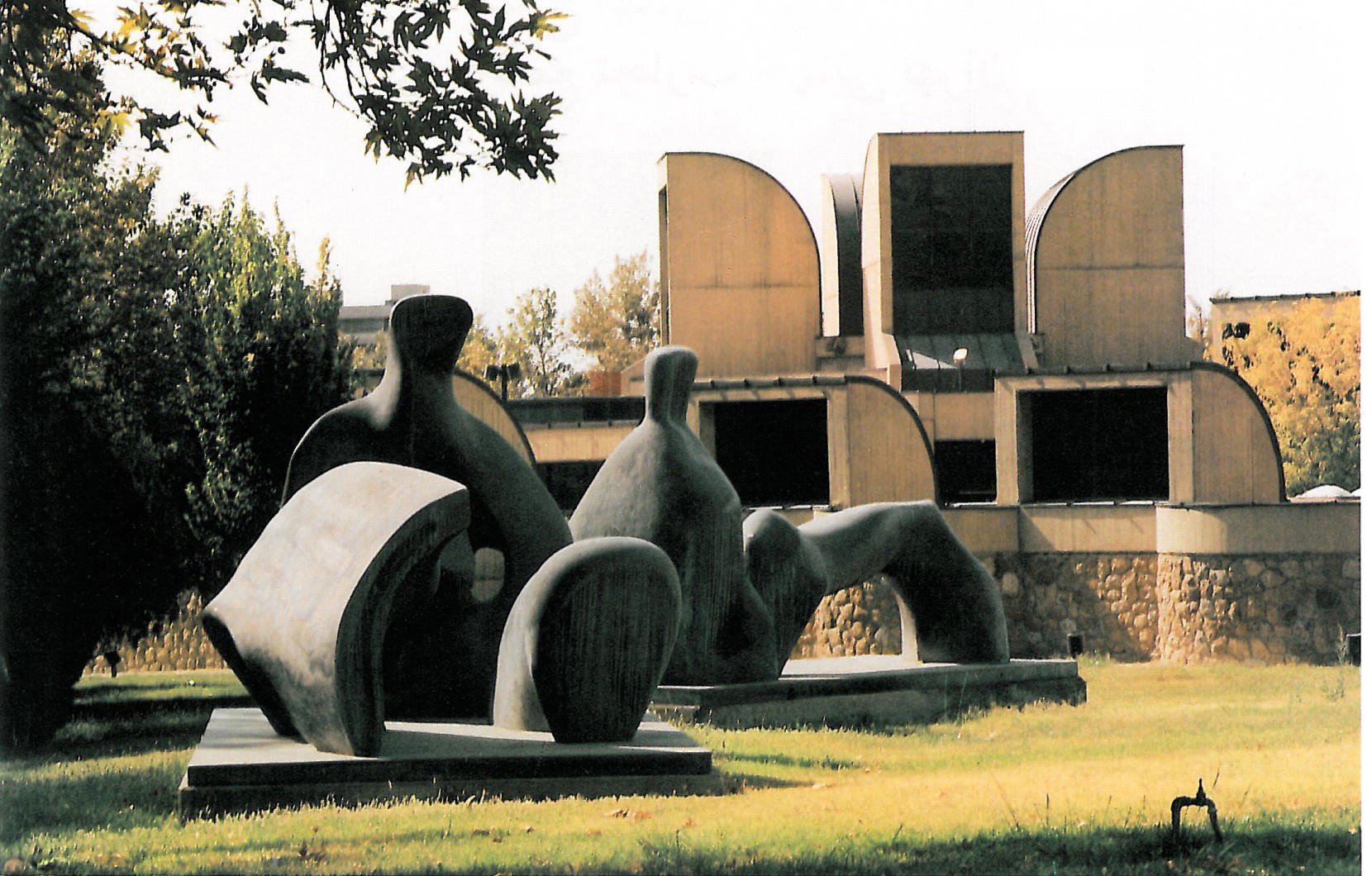Photograph of the Tehran Museum of Contemporary Art sculpture garden with three large Henry Moore reclining-figure bronze sculptures on the lawn under the museum's distinctive curved vault skylights