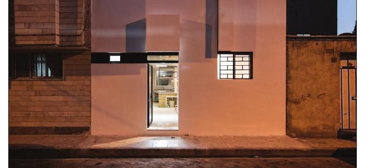 Pink dusk view of Aabaan Kitchen's white facade with the lit door slot drawing the eye into the kitchen
