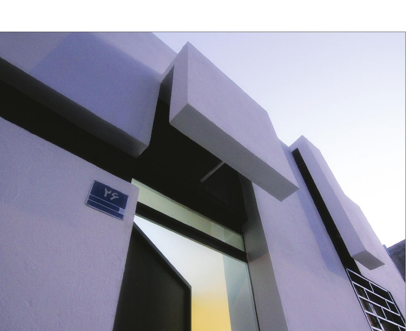 Close-up of the entrance with the projecting white volume cantilevered above the door and the No. 26 plate