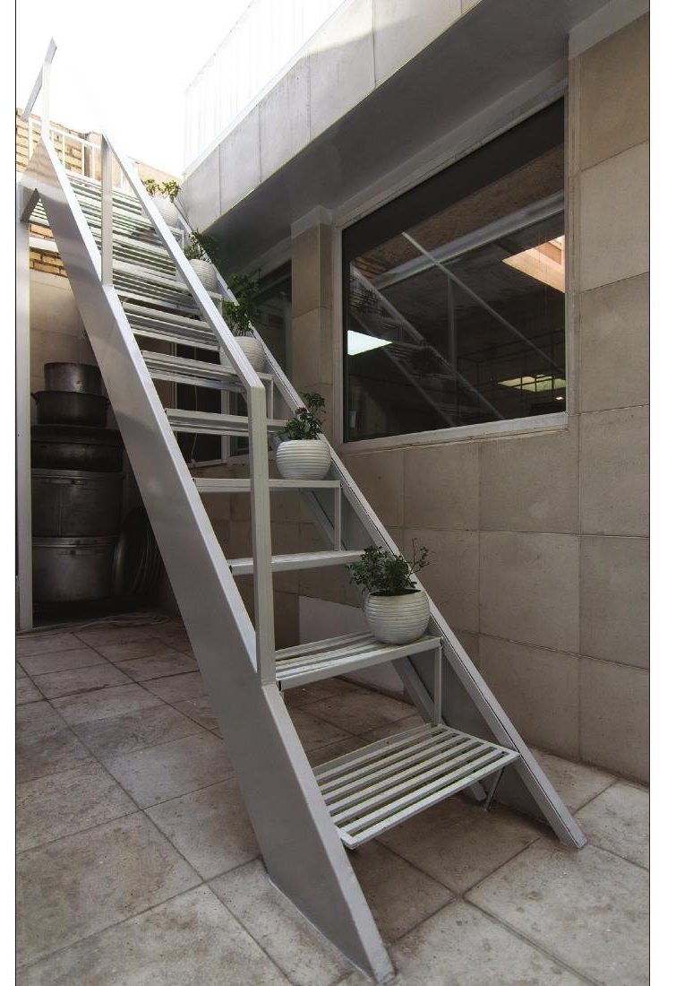 Aabaan Kitchen — light steel external stair leading up against the bare concrete wall, with a planter on each tread
