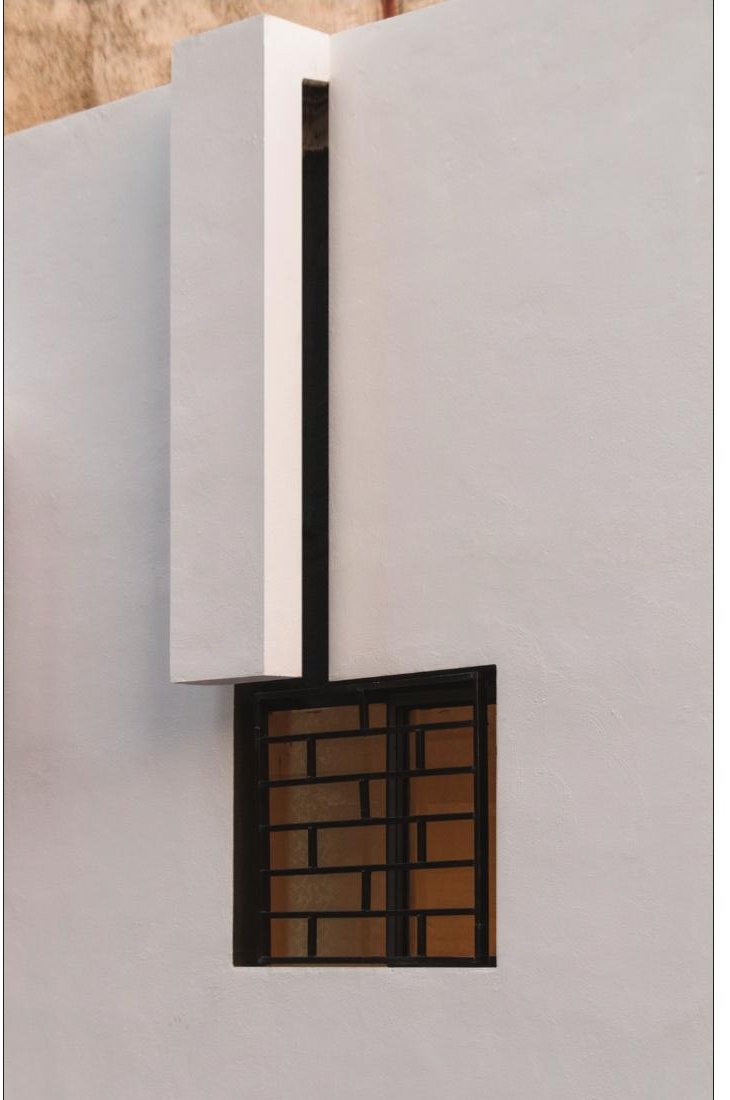 Detail of the white facade with a heavy projecting hood above a brick-and-iron-grille window