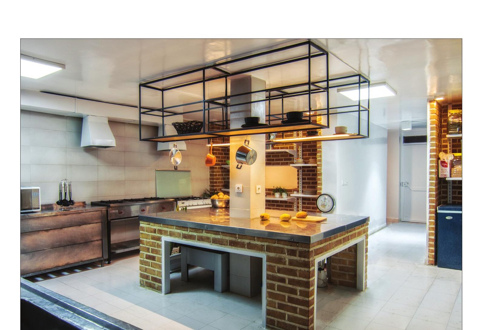Main view of Aabaan Kitchen's central work island with the steel hood and shelving cage suspended overhead