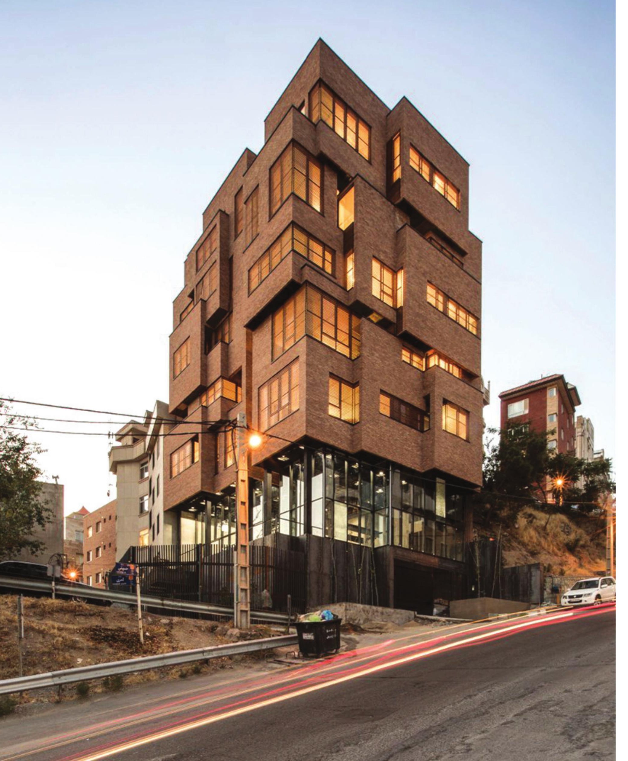 Darband House at dusk — stacked brick volume on the hill with car light trails