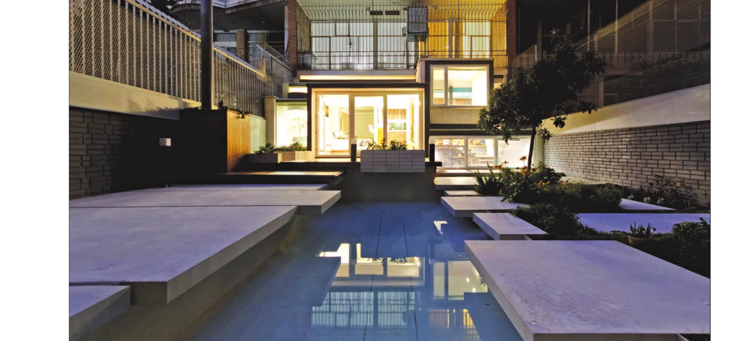 Rear courtyard of the House of Deflection at night with the pool and the lit glass volume above