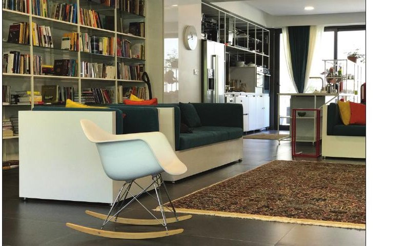 Manzarieh interior — a rocking chair and bookshelf next to a tall window in the open living room