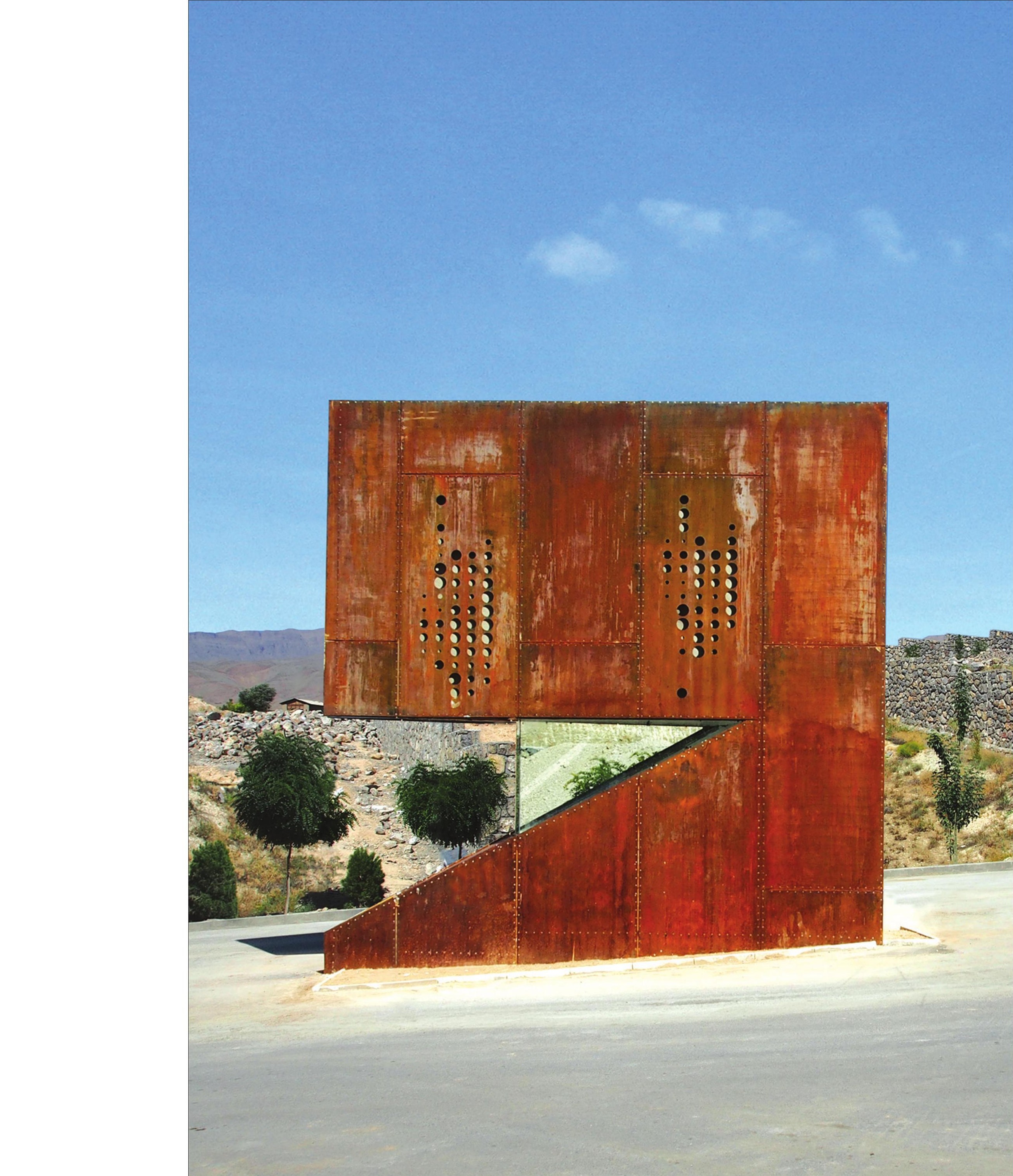 Corten guard kiosk on a stone platform overlooking the mountain road