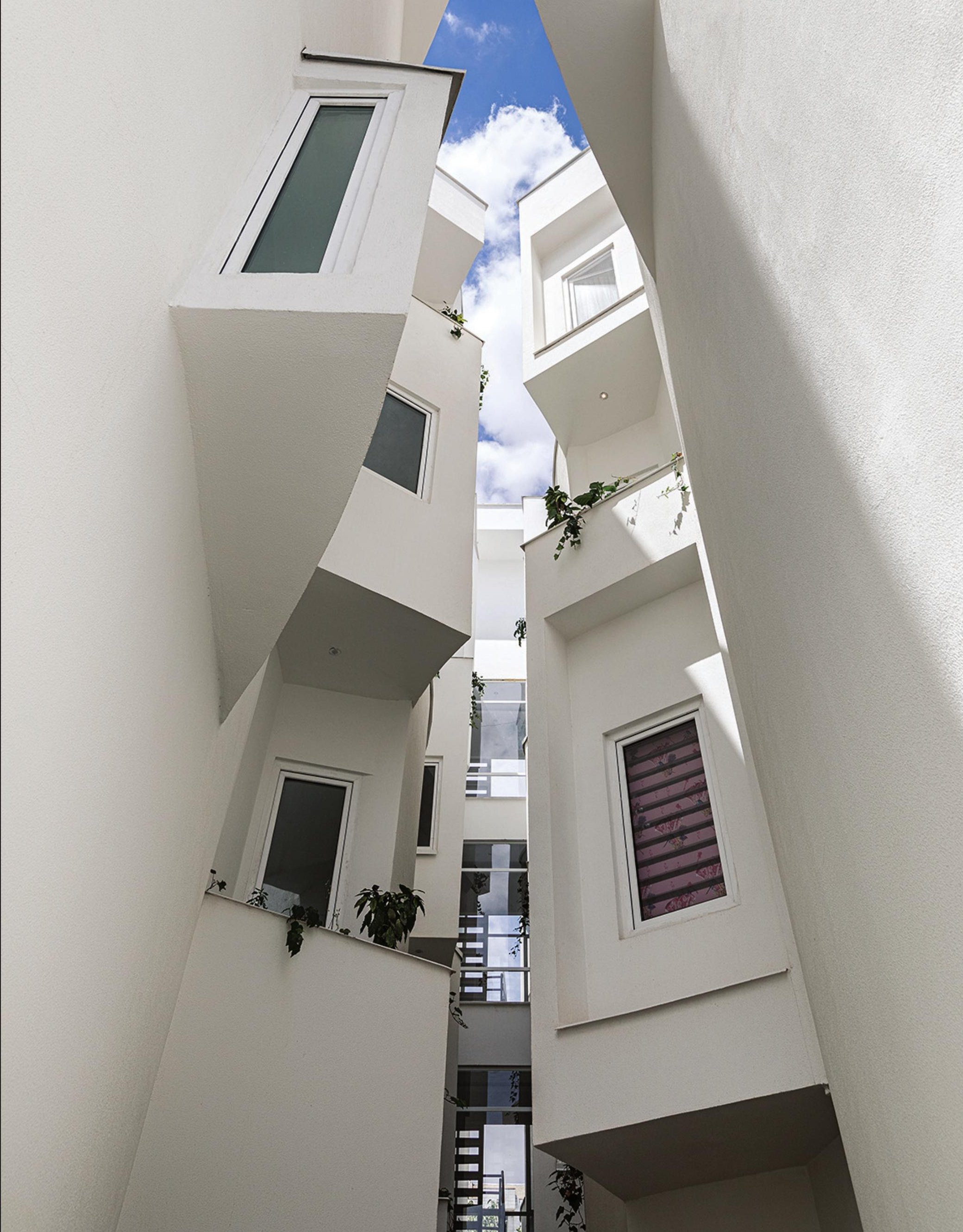 Vertical light-slit between two white volumes with sculptural projecting windows