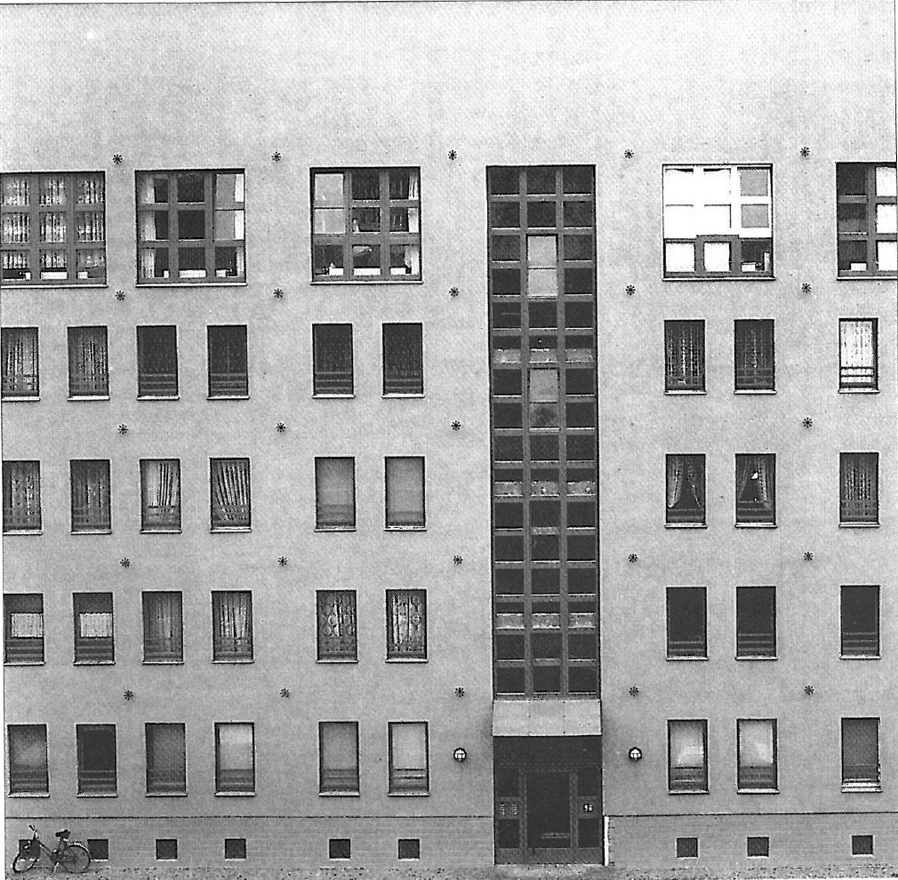 Photograph of twin gabled brick houses joined at a narrow vertical column, with rows of small dormer windows