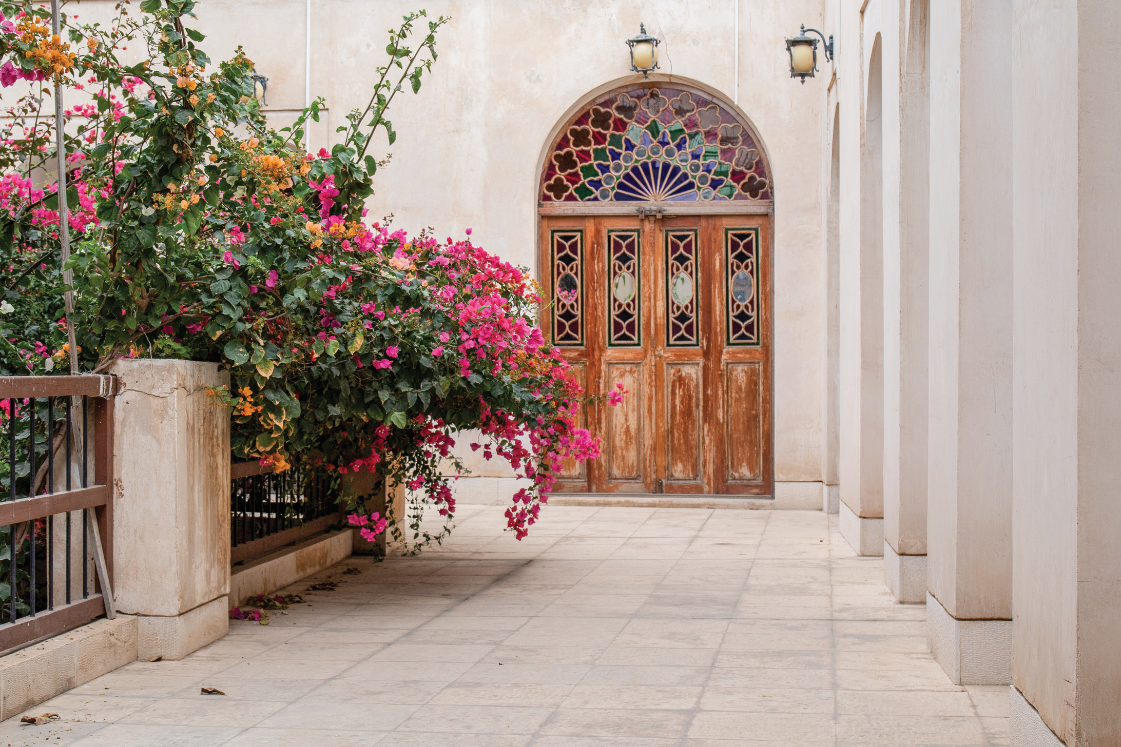 Arched wooden door with stained glass lunette and bougainvillea along the gallery