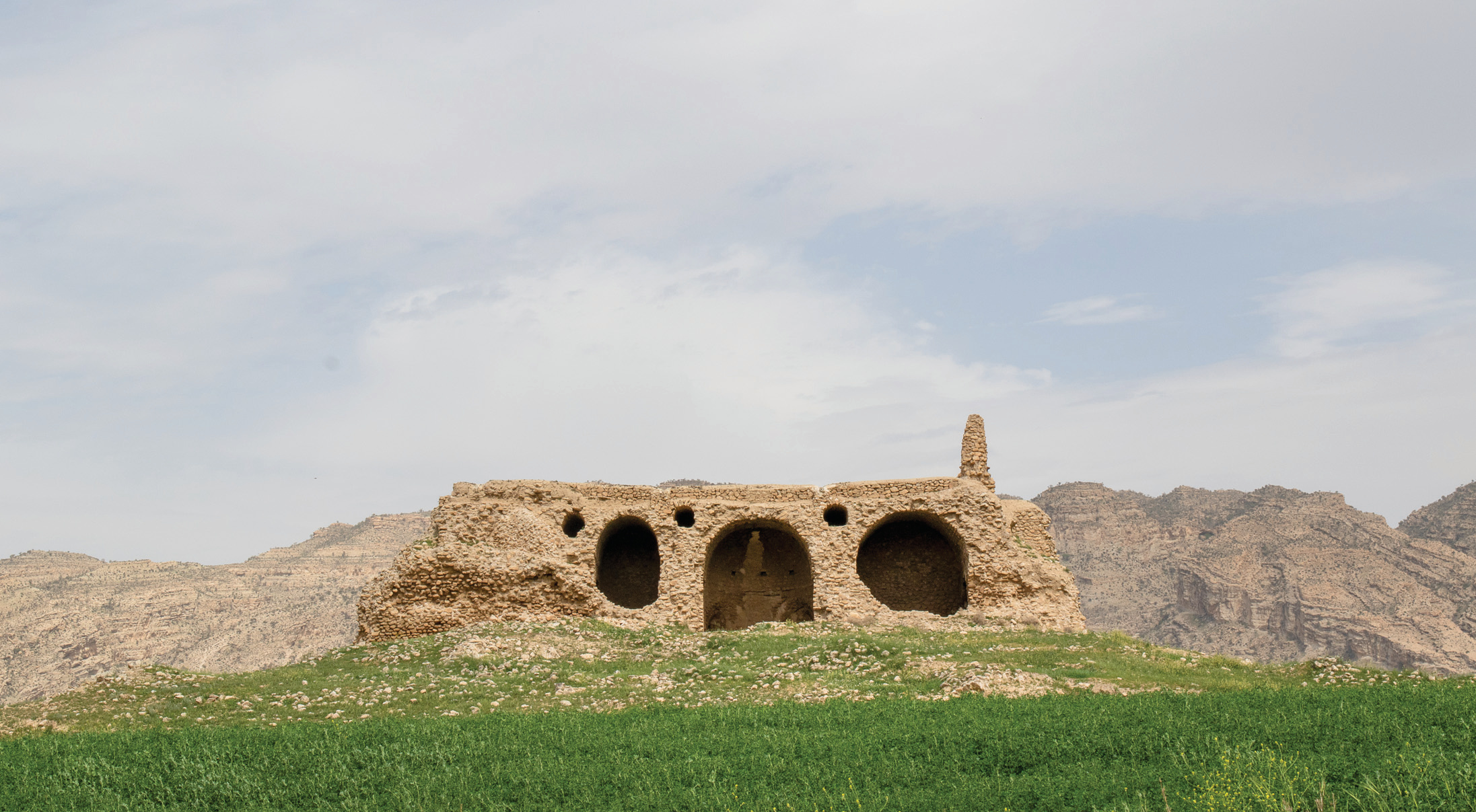 Ardashir Pavilion ruins on a green hilltop showing three large barrel-vaulted arches with mountains behind