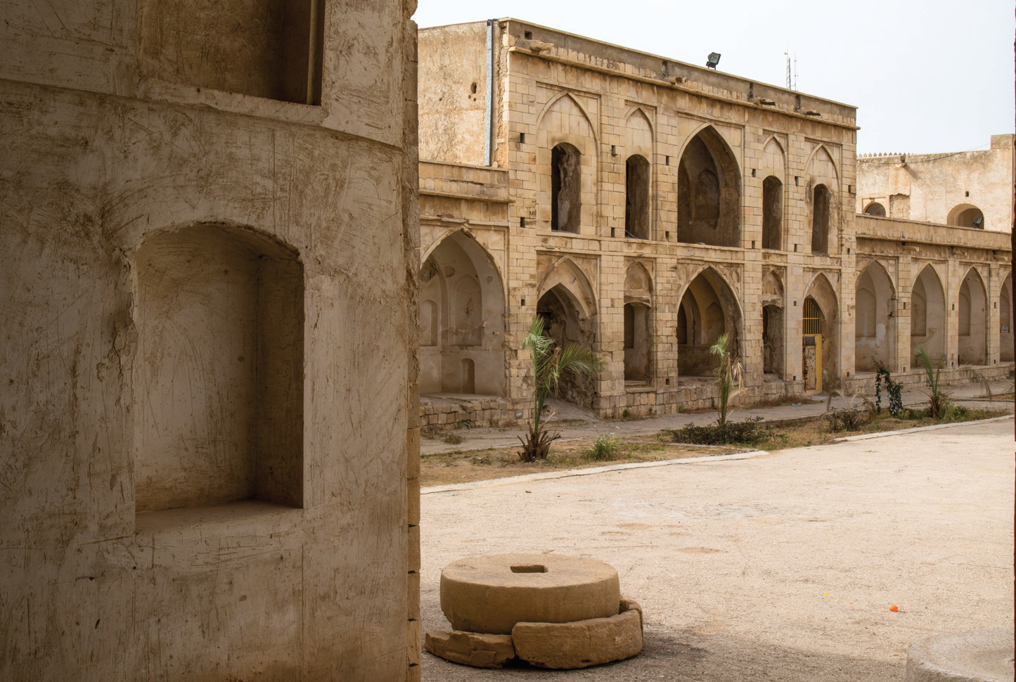 Courtyard detail showing two-story arcaded facade, corner tower, and a stone millstone in the foreground