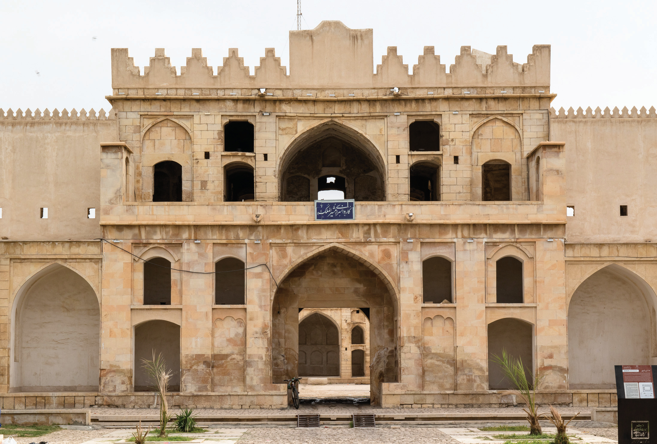 The grand entrance facade of the Borazjan Caravanserai with battlements, pointed arch portal, and arched niches