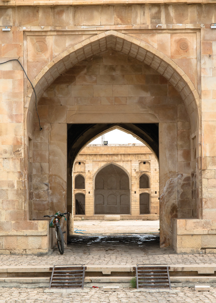 The pointed arch entrance portal of the Borazjan Caravanserai with dressed stone facade and a bicycle leaning against the wall
