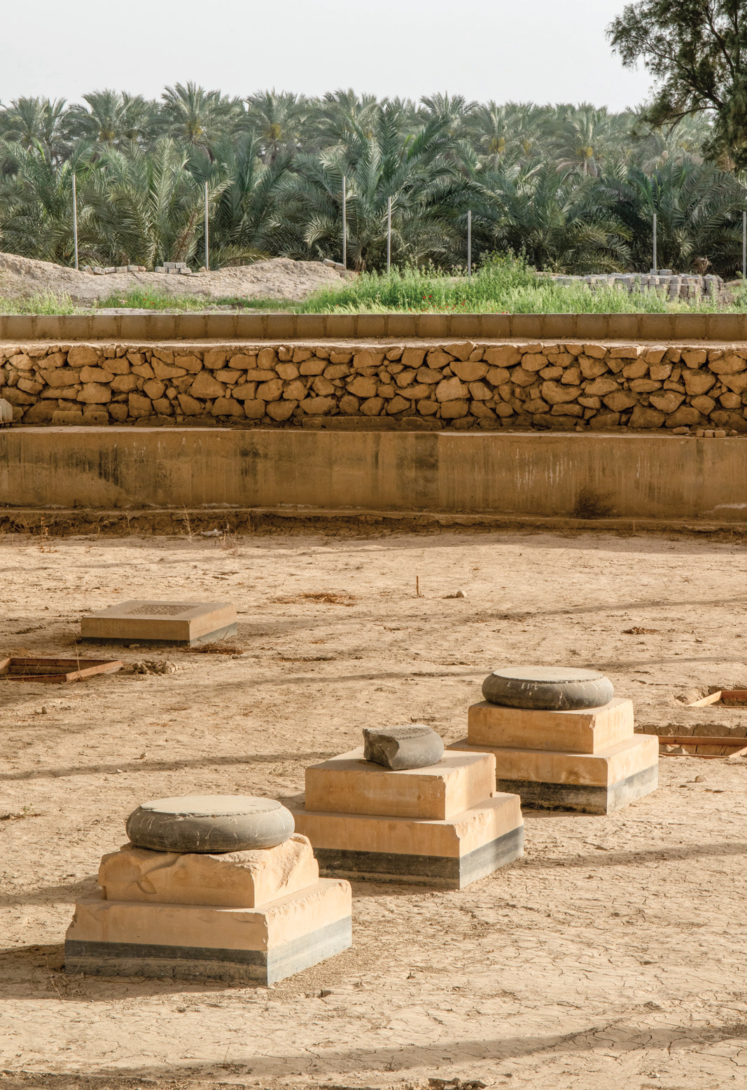 Close-up of Charkhab Palace column bases showing stepped black and cream stone construction with palm trees in the background