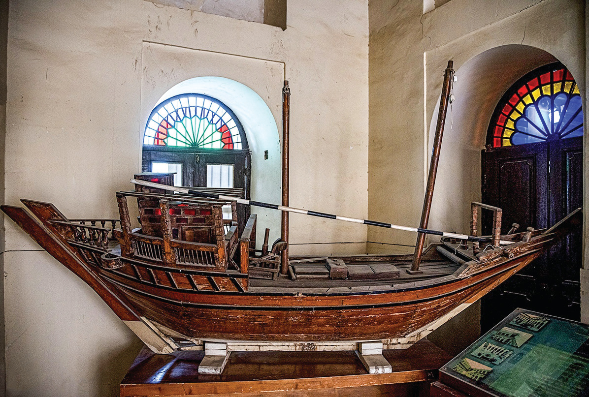 Scale model of a traditional dhow displayed between stained glass windows