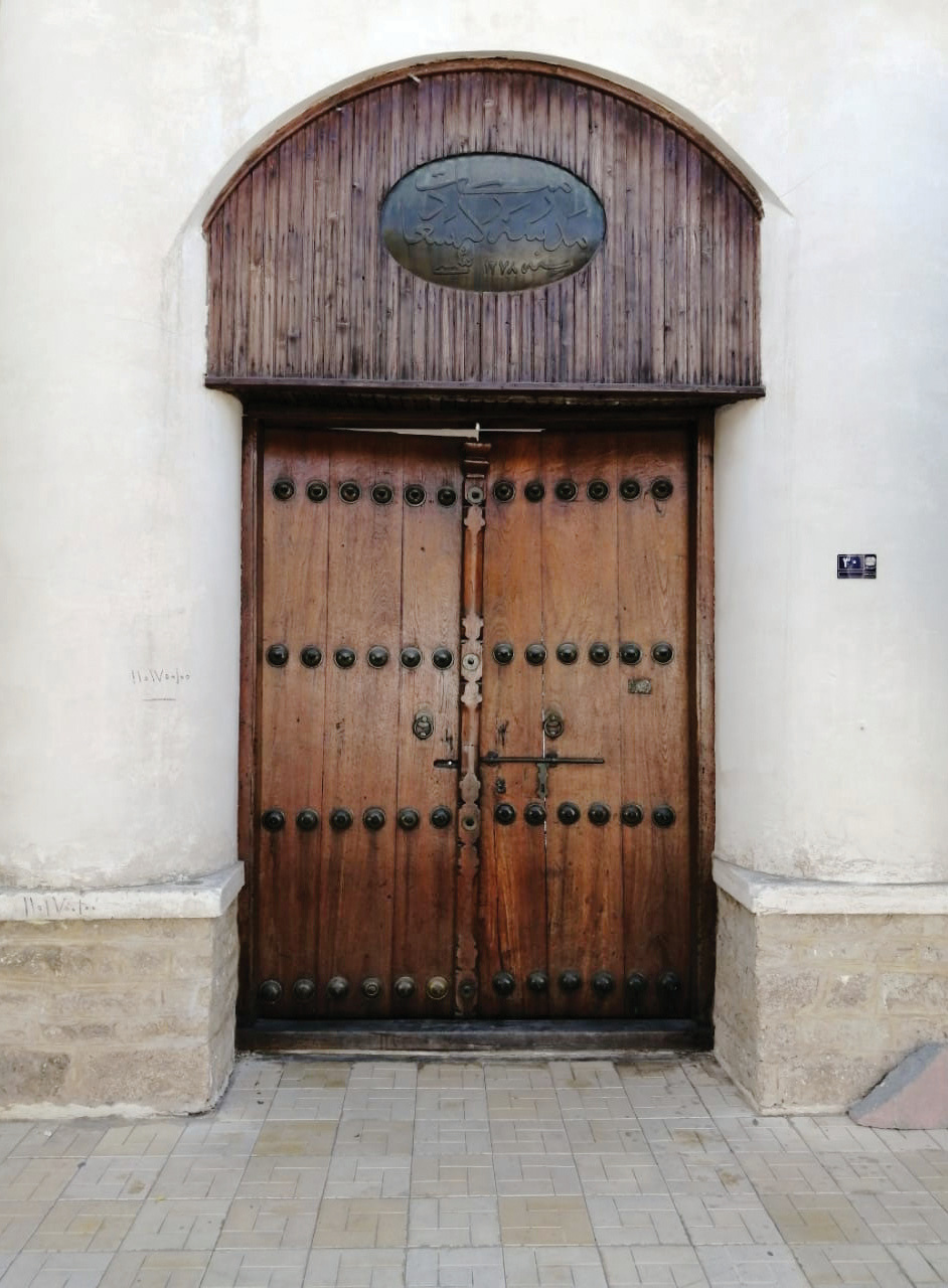 The studded wooden entrance door of the Saadat School with a plaque above