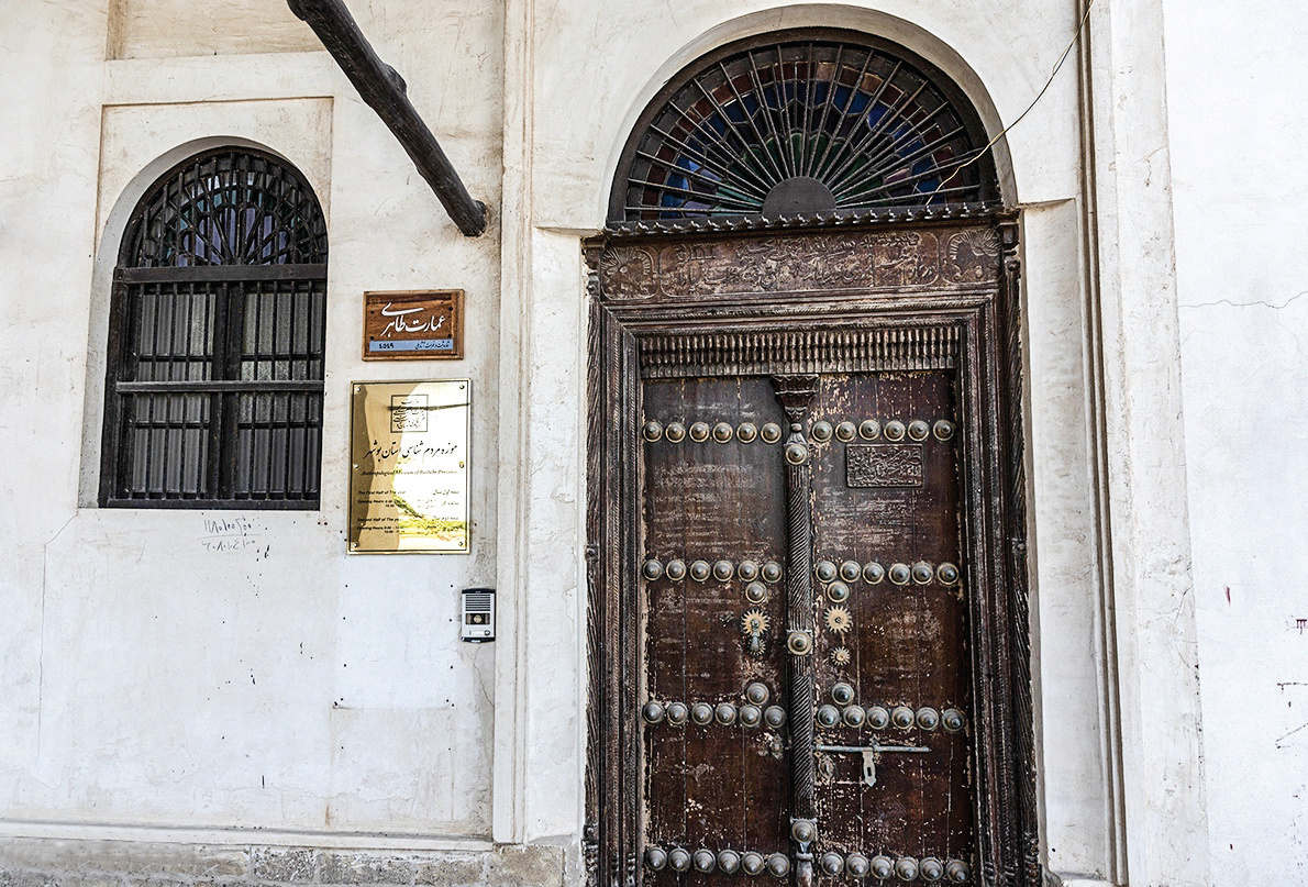 Ornate studded entrance door of the Amirieh Edifice with stained glass lunette above and museum signage