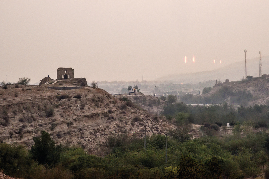 The fire temple on a hilltop with gas flares burning in the hazy distance — ancient and modern fire side by side