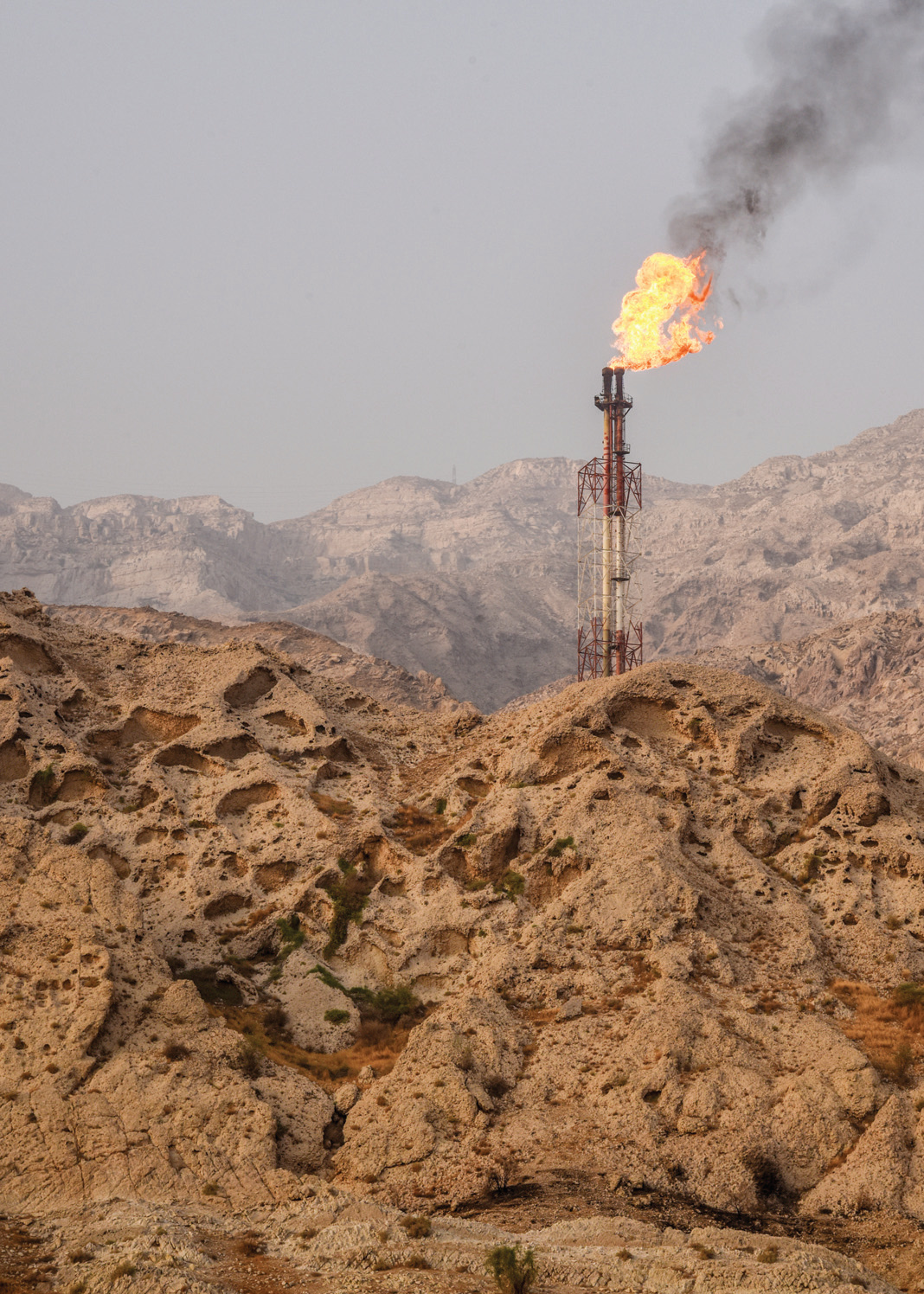 A gas flare burning against a rocky mountain backdrop