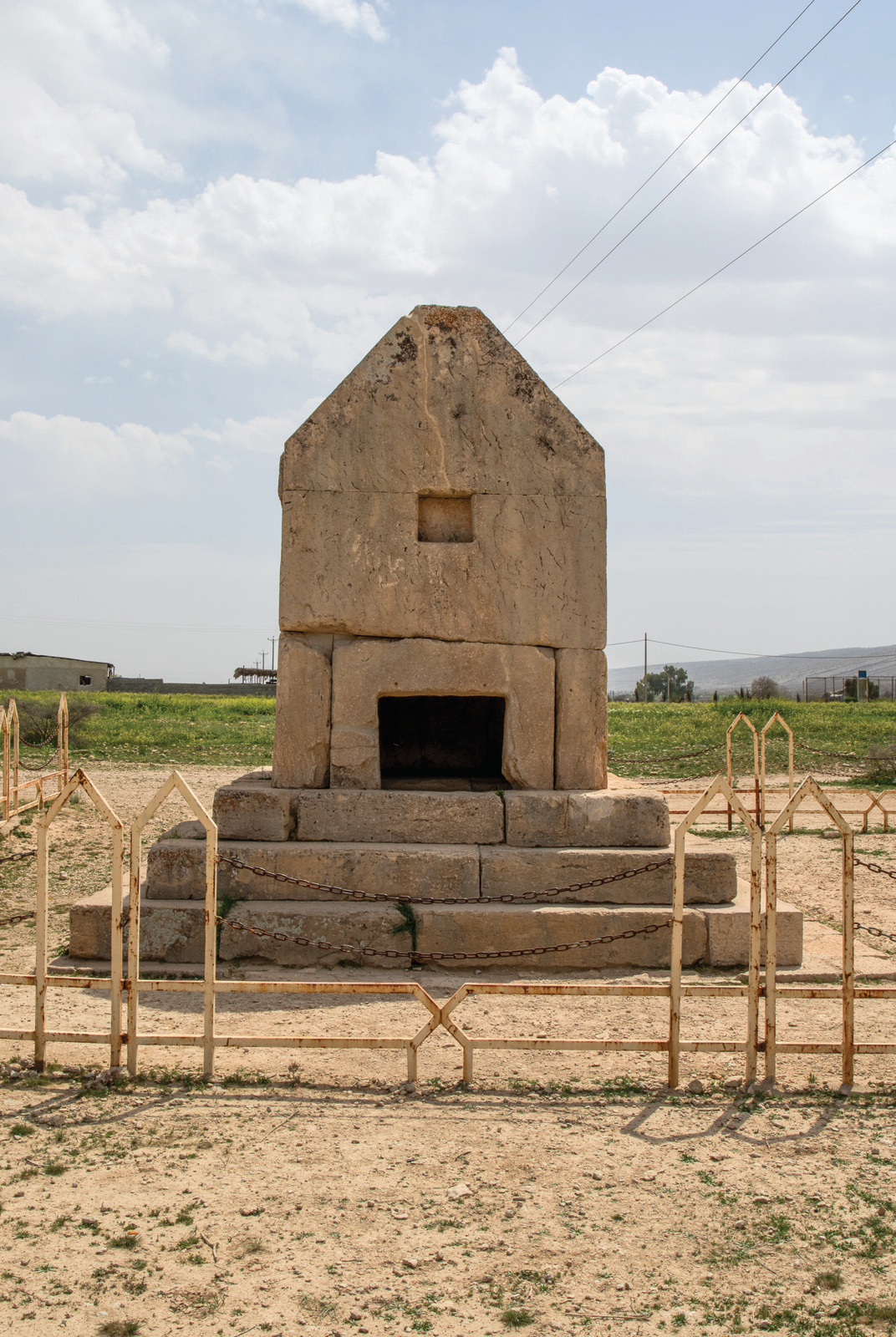 Front view of the Gor Dokhtar tomb — a rectangular stone structure with crescent-shaped roof, stepped base, entrance doorway, and iron fence