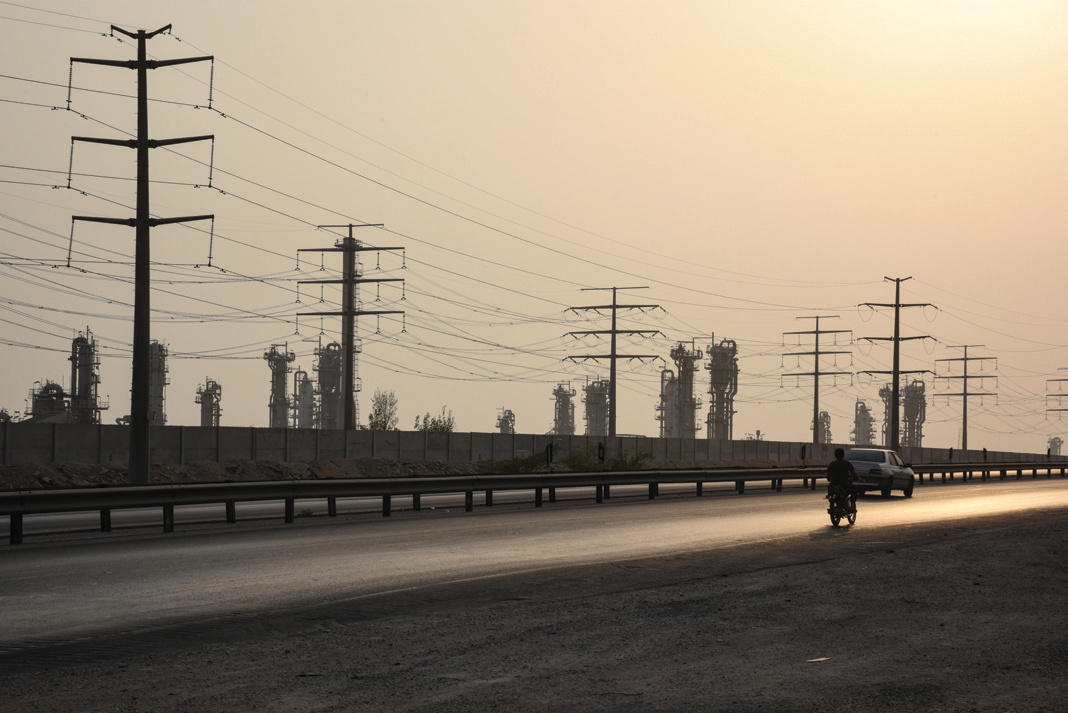 Highway alongside the petrochemical zone — power lines and refinery towers silhouetted against the hazy sky at dusk