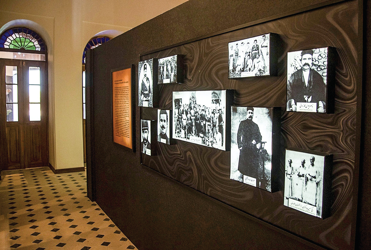 Gallery wall displaying historical black and white photographs of Bushehr notables on a dark marbled background