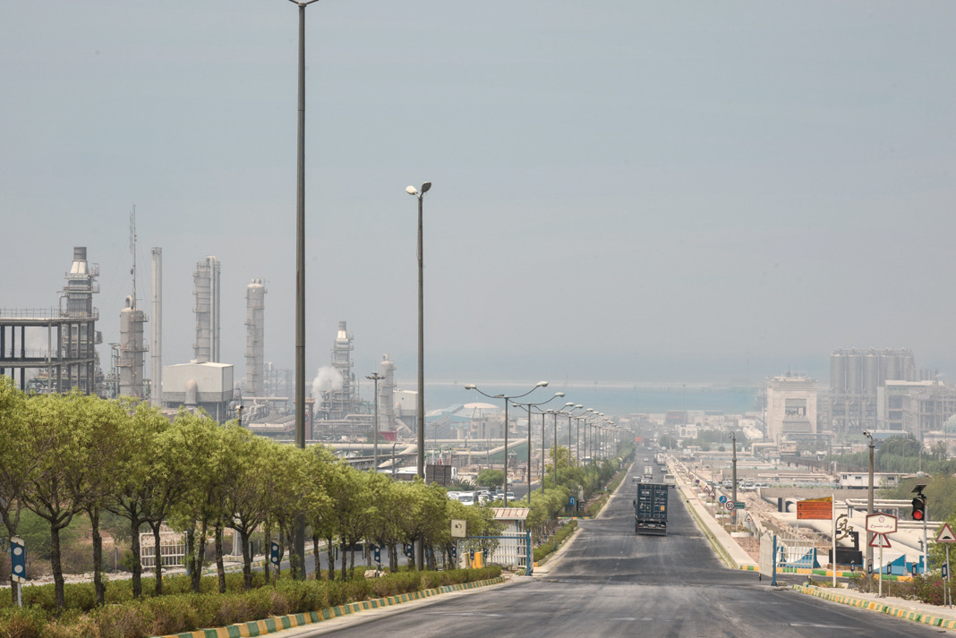 Road through the industrial zone with refinery towers looming in the hazy, polluted sky