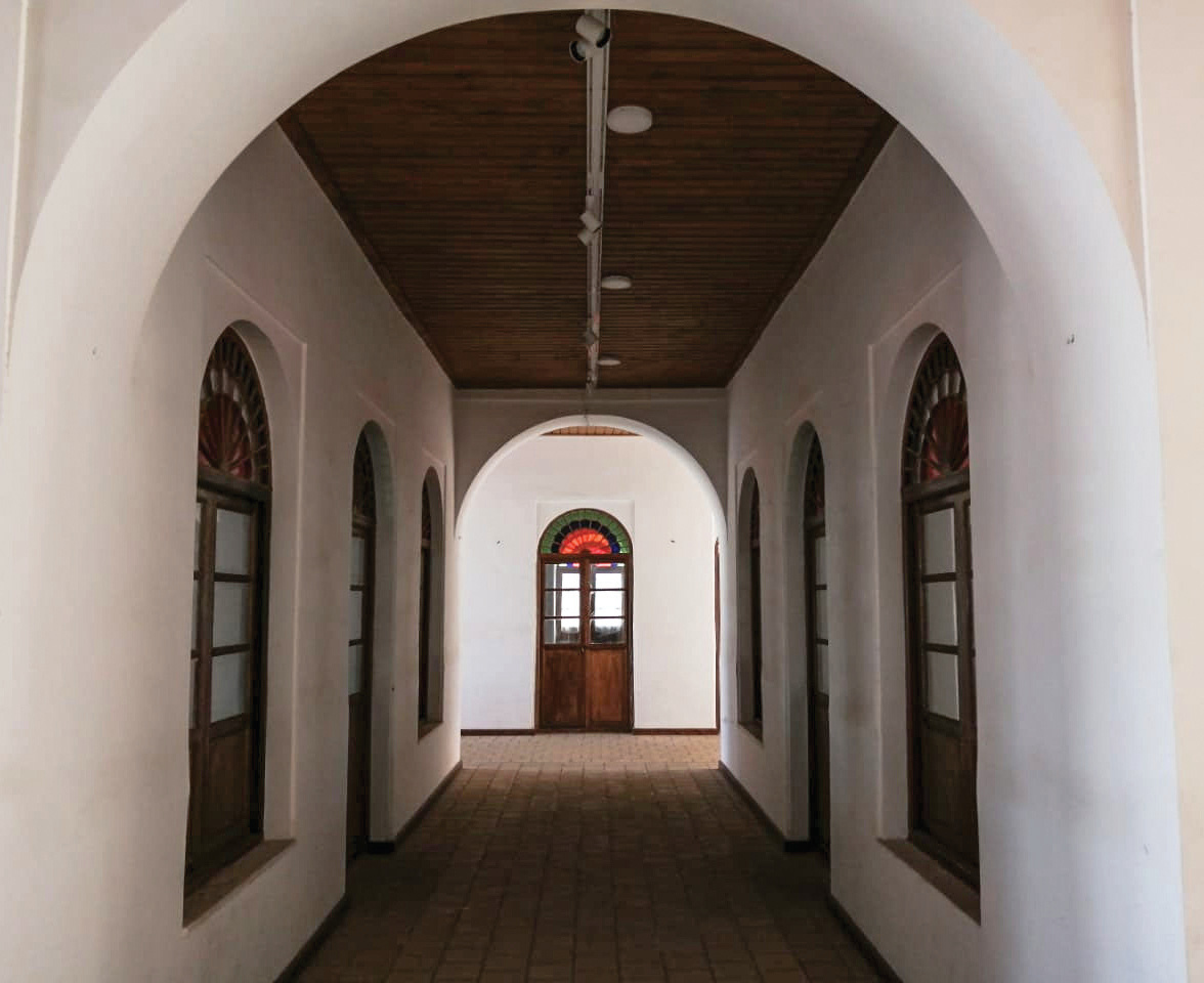 Interior corridor with arched ceiling, wooden doors on both sides, and a stained glass door at the end