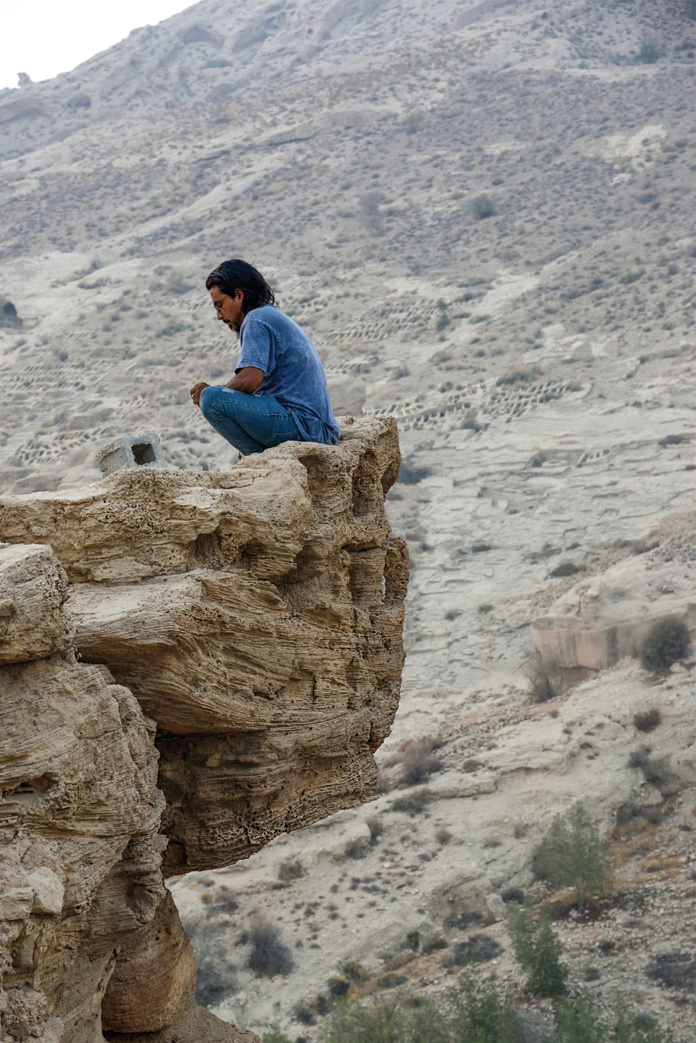 A man sitting on the edge of a rock cliff overlooking the Lir Valley with its stone basins visible on the hillside