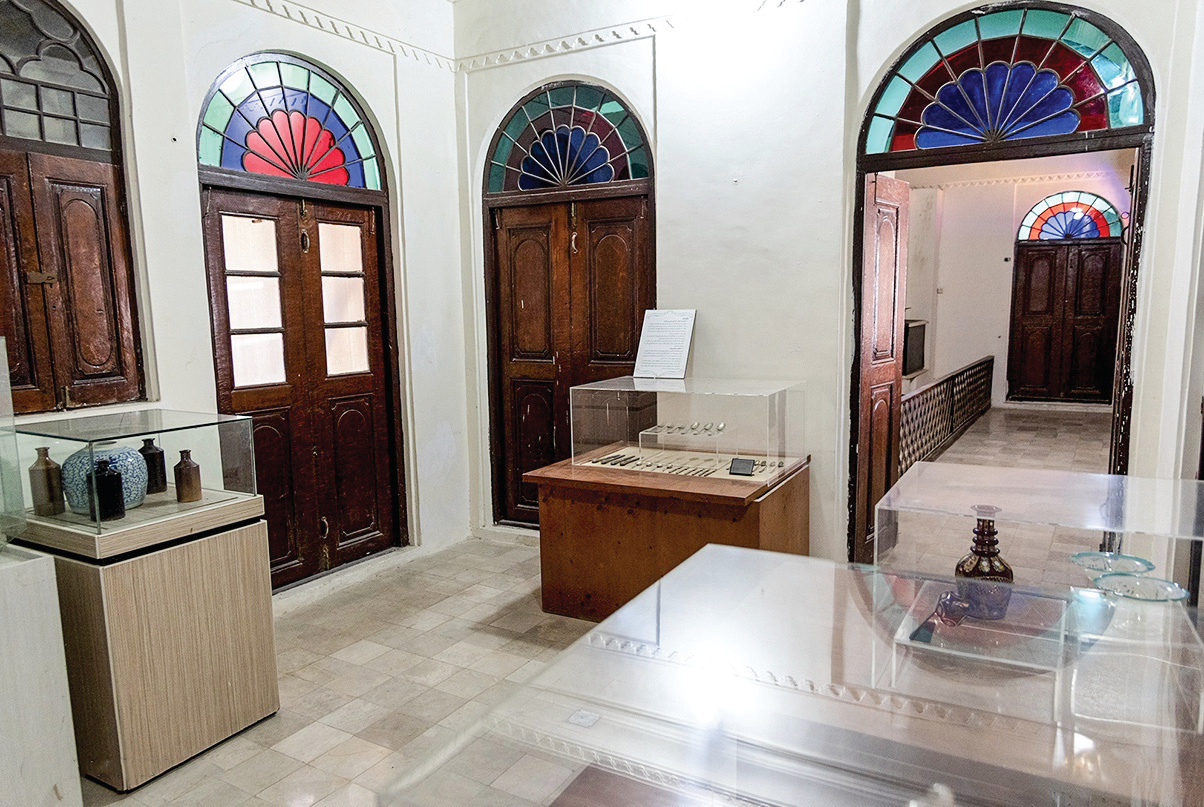 Museum room with three wooden doors featuring colorful fan-shaped stained glass lunettes and display cases