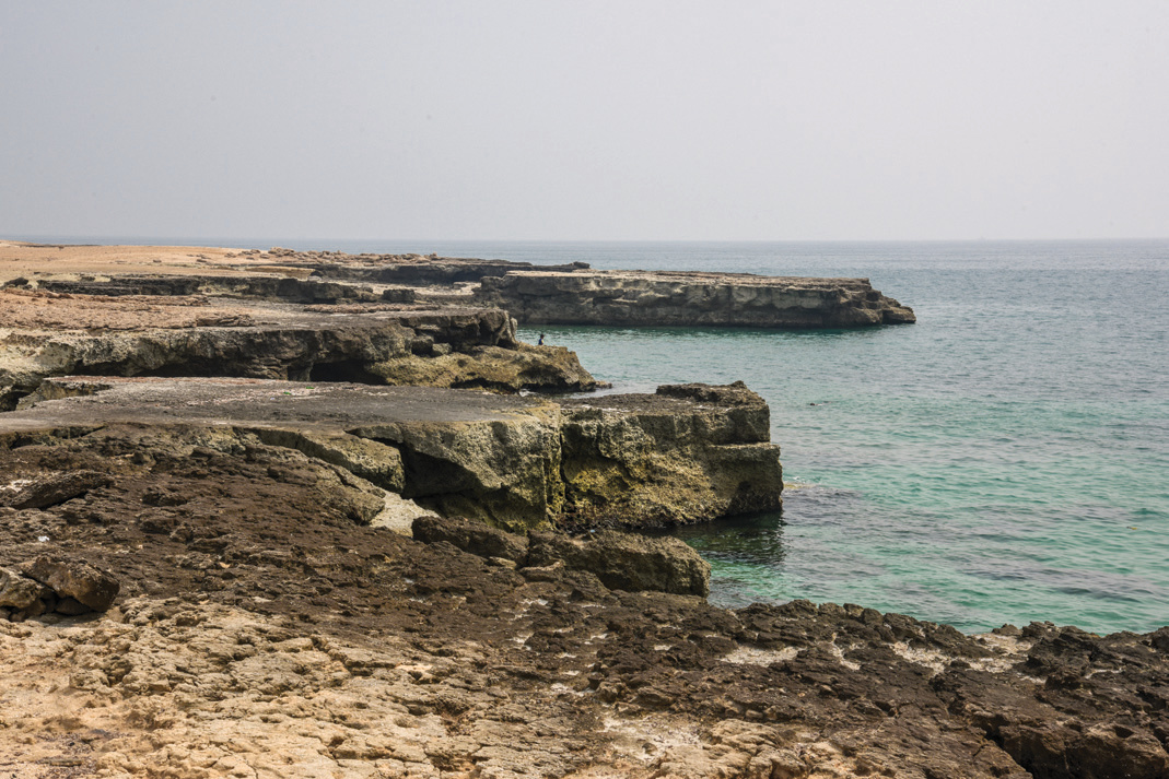 Rocky coastline of Nay Band cape with layered stone formations meeting the turquoise Persian Gulf