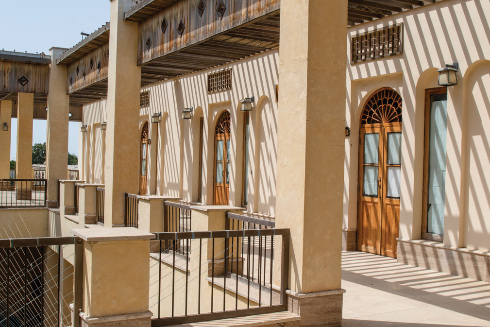 Gallery corridor of the new building with arched doors, timber pergola, and strong shadow patterns
