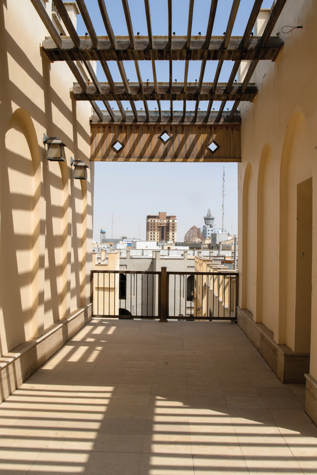 Open terrace framing a view of the Bushehr city skyline with timber pergola and arches