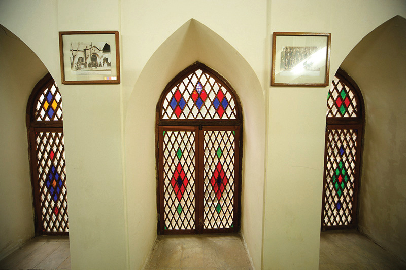 Three pointed-arch orosi windows with stained glass diamond patterns and historical photographs above