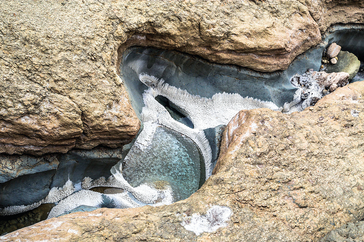A salt-encrusted pool nestled within a rock crevice, showing blue-gray mineral deposits