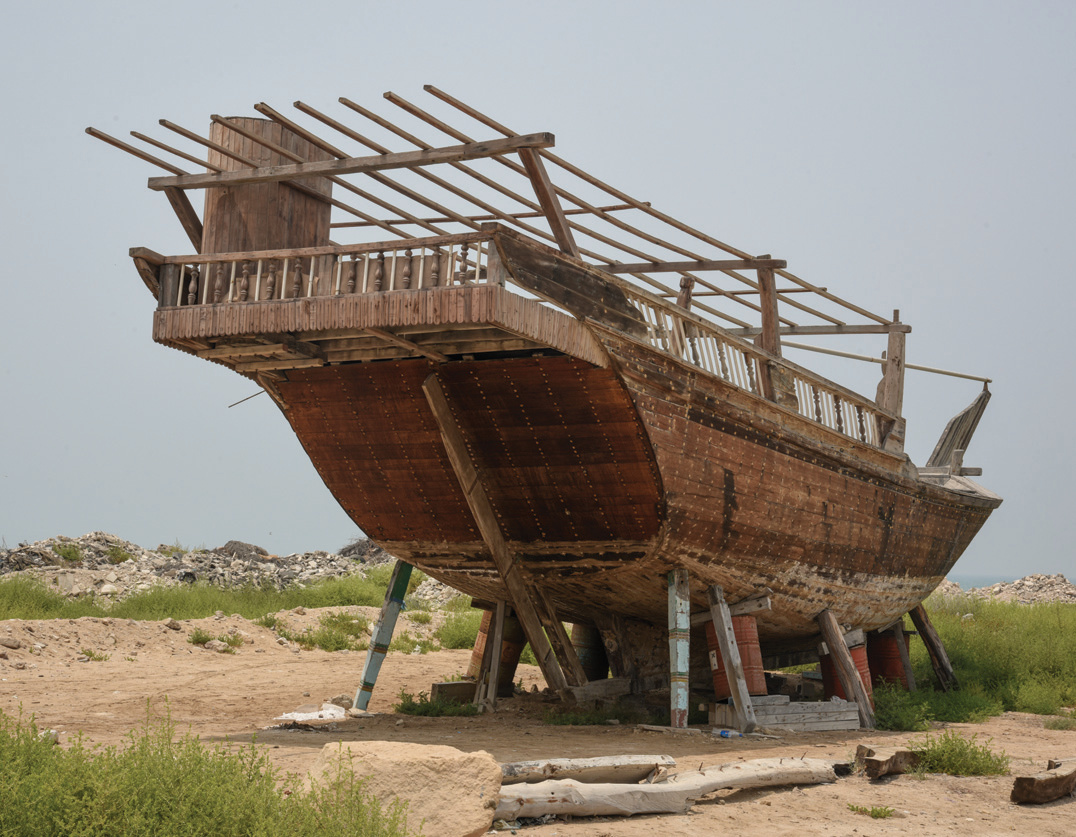 A traditional wooden dhow under construction on the shore near Asaluyeh