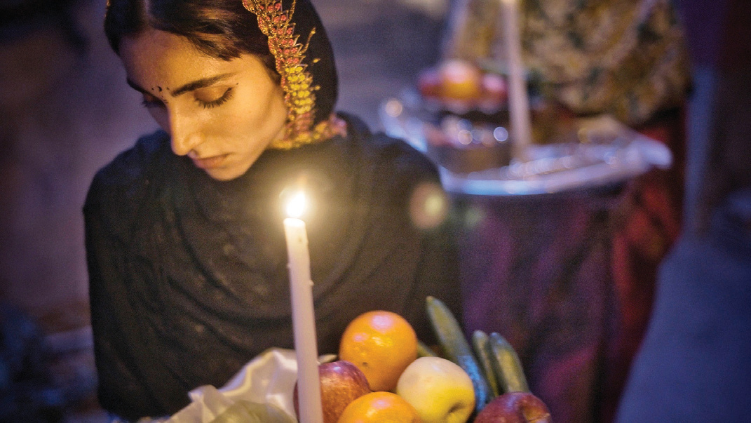Young woman holding a tray of fruit and a lit candle during Zar ceremony preparations
