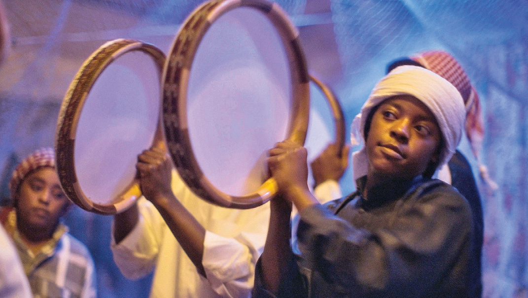 Young Afro-Iranian boys playing large traditional drums (dohol) during a Zar ceremony, wearing turbans