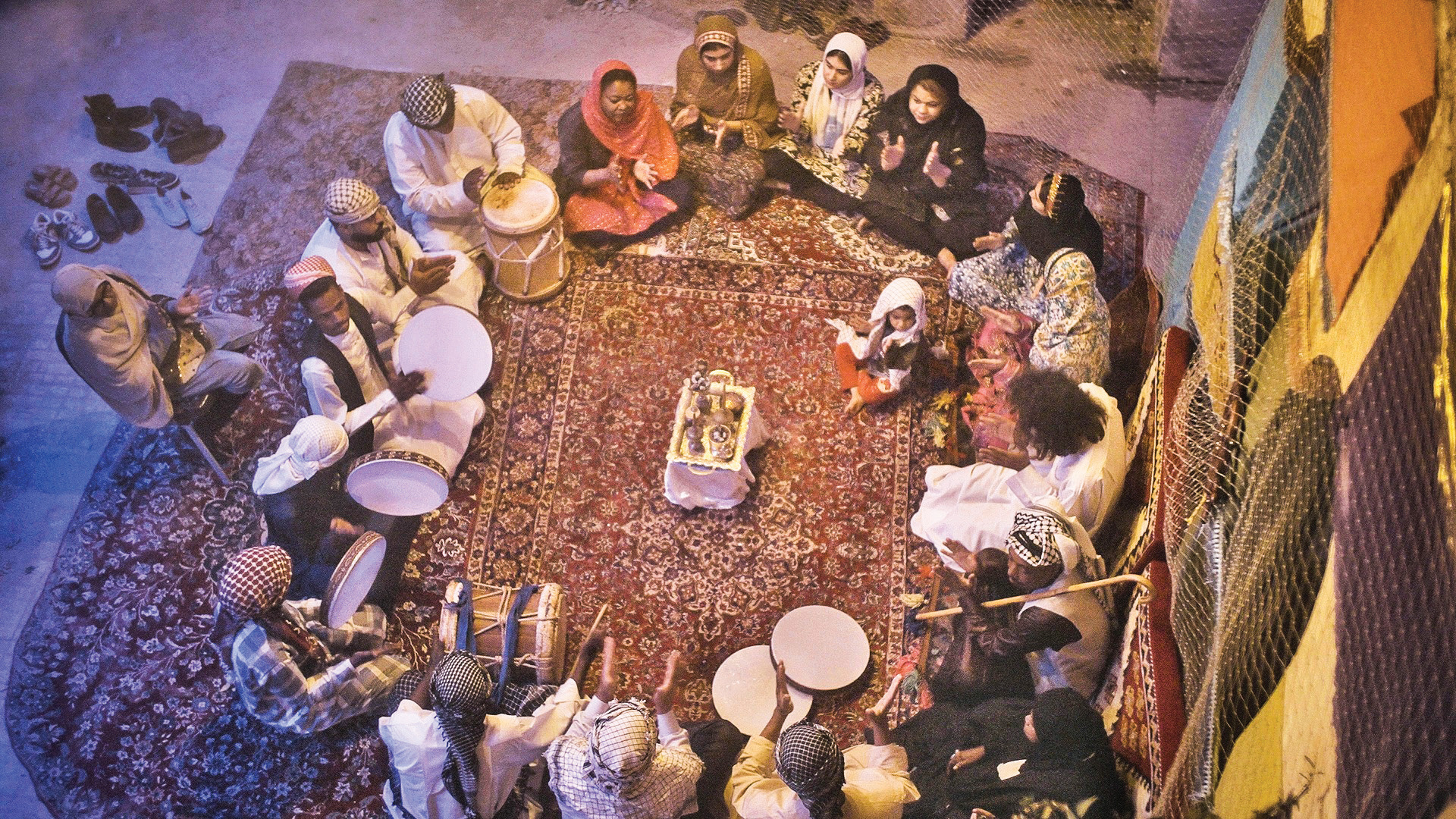 Overhead view of a Zar ceremony: participants sitting in a circle on a carpet, with drums and ritual objects in the center