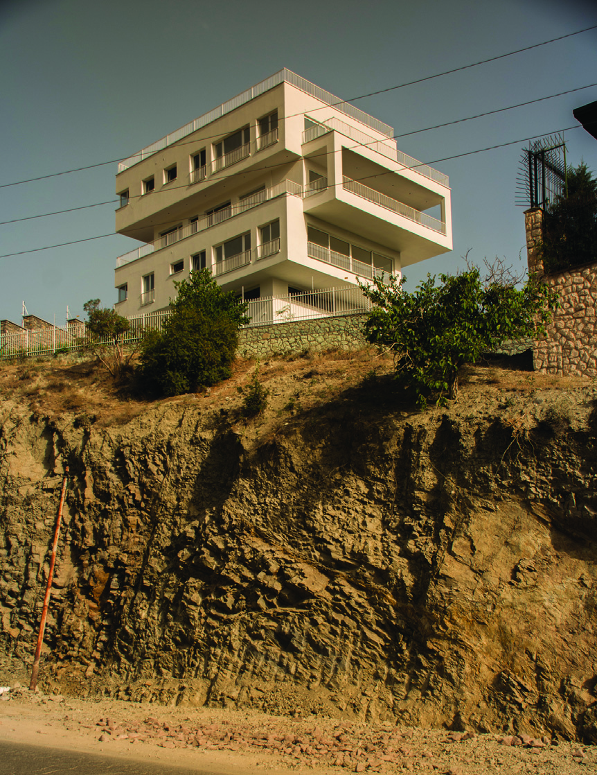 View of the building from the road below showing it rising from the exposed rock cliff with its angular white volumes