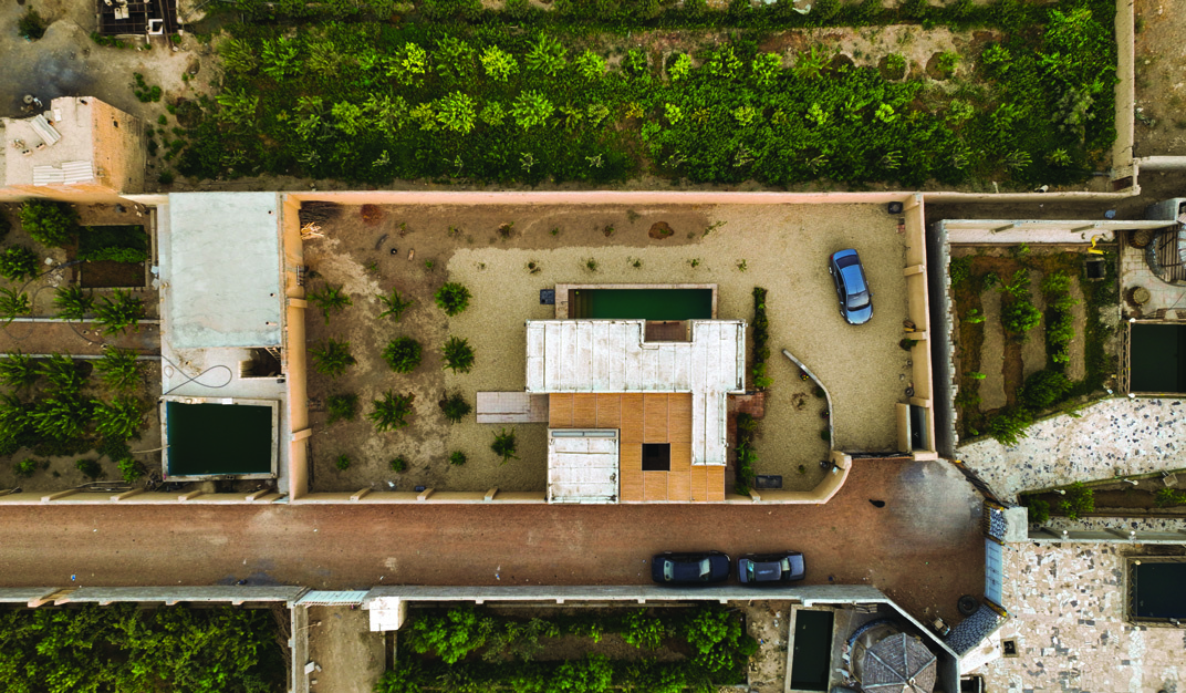 Top-down aerial view of Khaki House showing the compact built footprint within a large walled garden plot, with orchards and a road visible